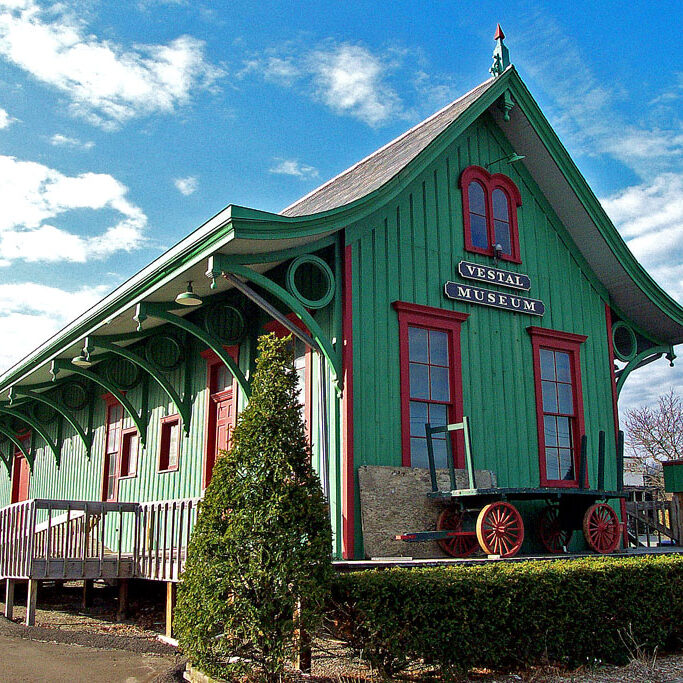 A green wooden museum building with red window frames and a covered entrance deck.